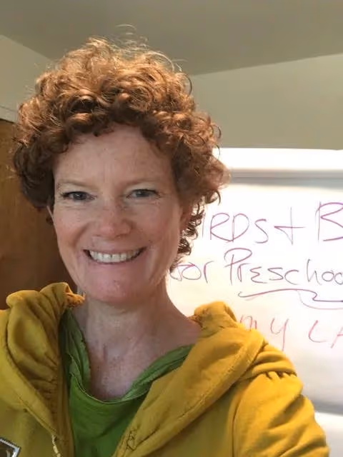 Amy Lang is shown wearing a yellow sweatshirt and green shirt in front of a whiteboard where she's been brainstorming.