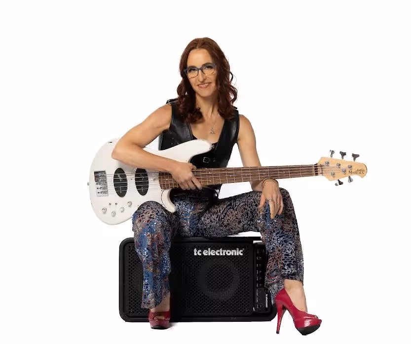 Ariane Cap sits on a speaker while holding an electric guitar.